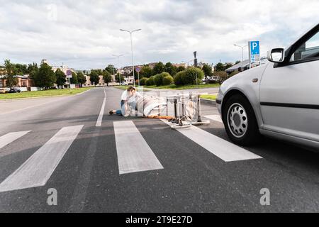 Schockierte Mutter auf dem Gehweg nach einem Autounfall, als das Fahrzeug ihren Kinderwagen traf. Konzepte von Sicherheit, Verkehrsordnung und Versicherung. Stockfoto