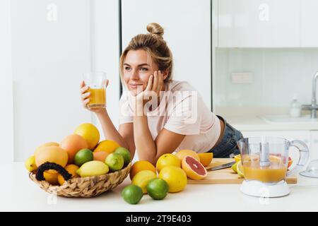 Junge Frau, die frisch gepressten, selbstgemachten Orangensaft in der weißen Küche trinkt Stockfoto