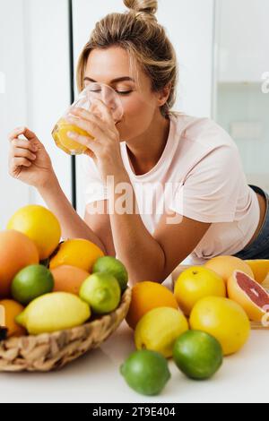 Junge Frau, die frisch gepressten, selbstgemachten Orangensaft in der weißen Küche trinkt Stockfoto