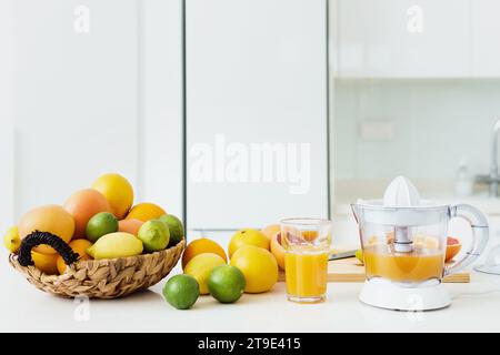 Glas Orangensaft, Zitruspresse und verschiedene Zitrusfrüchte auf weißem Küchentisch Stockfoto