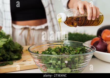 Nahaufnahme der weiblichen Hand, die extra natives Olivenöl zu vegetarischem Salat hinzufügt Stockfoto