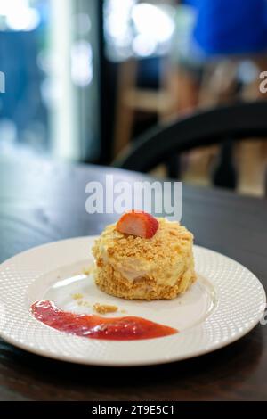 Napoleonkuchen mit Schichten Puffcreme und Krümeln mit Erdbeere oben und Sauce auf dem Teller Stockfoto