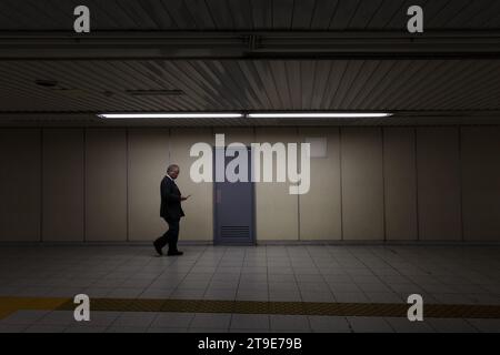 Ein japanischer Angestellter oder Büroangestellter überprüft sein Klapptelefon, während er in Passagen unter dem Bahnhof Tokio läuft. Tokio, Japan. Stockfoto