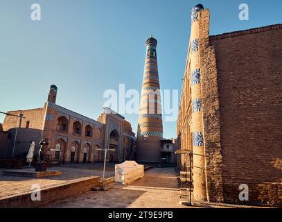 Alter mittelalterlicher Platz und Flötistenstatue und hohes Minarett auf dem Platz in Itchan Kala, der antiken Stadt Chiwa in Usbekistan. Stockfoto