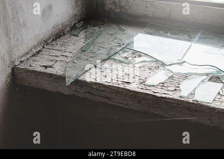 Nahaufnahme einer schäbigen Fensterbank in einem verlassenen Gebäude mit Spinnennetz und Glasscherben. Stockfoto