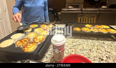 Pheonix, Arizona, USA. November 2023. Zu den Vorbereitungen für Hannukah durch eine jüdische Familie in Phoenix, Arizona, gehört die Herstellung von Latkahs, auch bekannt als Kartoffelpfannkuchen, ein Essen, das traditionell am jüdischen Lichterfest gegessen wird. Ein Starbucks-Becher ist im Zentrum: Der Koch brauchte einen dringend benötigten Boost aus Koffein, nachdem er sich auf Thanksgiving vorbereitet hatte und dann in eine frühe Hanukkah einsetzte, während die Familie zusammen war. (Kreditbild: © Amy Katz/ZUMA Press Wire) NUR REDAKTIONELLE VERWENDUNG! Nicht für kommerzielle ZWECKE! Stockfoto