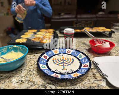 Pheonix, Arizona, USA. November 2023. Zu den Vorbereitungen für Hannukah durch eine jüdische Familie in Phoenix, Arizona, gehört die Herstellung von Latkahs, auch bekannt als Kartoffelpfannkuchen, ein Essen, das traditionell am jüdischen Lichterfest gegessen wird. Ein Teller mit 'Happy Hanukkah' ist in der Mitte. Dahinter befindet sich ein Starbucks-Becher im Zentrum: Der Koch brauchte einen dringend benötigten Schub aus Koffein, nachdem er sich auf Thanksgiving vorbereitet hatte und dann zu einem frühen Hanukkah startete, während die Familie zusammen war. (Kreditbild: © Amy Katz/ZUMA Press Wire) NUR REDAKTIONELLE VERWENDUNG! Nicht für kommerzielle ZWECKE! Stockfoto