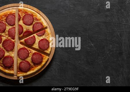 Pepperoni-Pizza italienische, in sechs Stücke geschnittene Pizza auf Holzständer, dunkler Hintergrund von oben, mit Platz zum Kopieren von Text. Stockfoto