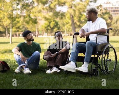 Eine Gruppe von verschiedenen männlichen Freunden, einer von ihnen im Rollstuhl, der sich im Park miteinander redet. Freundschaft, Behinderung Stockfoto