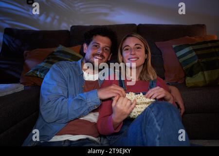 Junge kaukasische Paare, die sich zu Hause im Wohnzimmer ausruhen und abends gemeinsam einen Film anschauen. Stockfoto