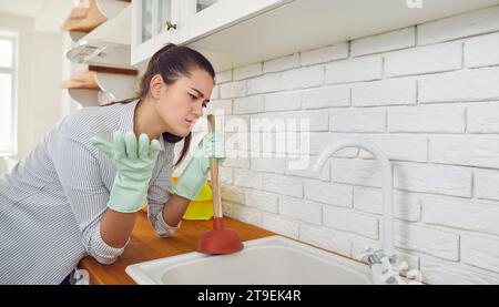 Frau, die am Haus arbeitet und versucht, die Blockade in der Küchenspüle zu beseitigen Stockfoto