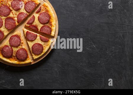 Pepperoni Pizza in Stücke geschnitten auf Holzbrett, auf dunklem Hintergrund mit Platz zum Kopieren von Text. Stockfoto