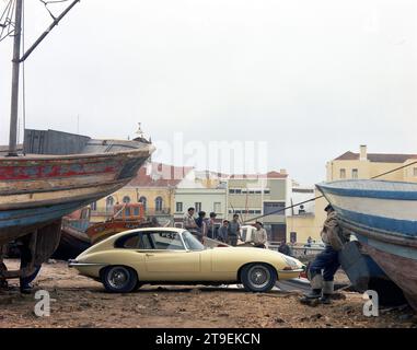 1966 Cream Jaguar E-TYPE, Serie 1, 2+2, im portugiesischen Fischereihafen mit Fischerbooten und Männern Stockfoto