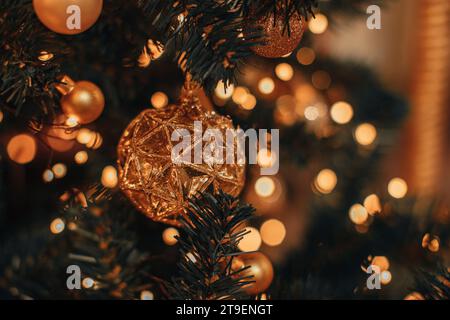 Goldene, glänzende Weihnachtskugel hängt an einem Weihnachtsbaum mit goldenen Lichtern. Dekorierte Fichtenzweige Stockfoto