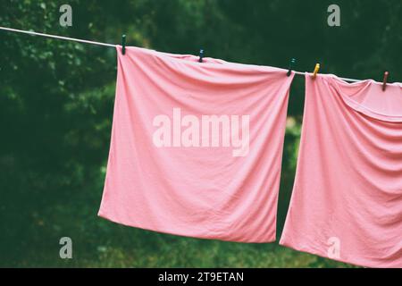 Rosafarbene Kissenbezüge werden im Garten an einem Seil mit Plastiktüchern getrocknet. Stockfoto