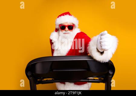 Foto von aktiver energetischer santa claus tragen Sonnenbrille Hut laufen newyear Party Sportausrüstung isoliert auf gelbem Hintergrund Stockfoto