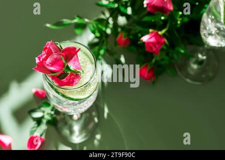 Köstliches erfrischendes Sektgetränk mit Zitrone und Rosen auf grünem Hintergrund. Sekt mit Blumen und Limette mit Rosenzitronenspritzer Stockfoto