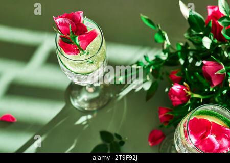 Köstliches erfrischendes Sektgetränk mit Zitrone und Rosen auf grünem Hintergrund. Sekt mit Blumen und Limette mit Rosenzitronenspritzer Stockfoto