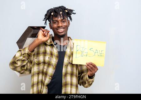 afrikanischer schöner Mann mit Einkaufstasche und gelber Karte mit Big Sale-Aufschrift. Black Friday Stockfoto