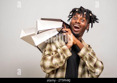 Afrikanischer Mann mit Handtaschen, aufgeregt nach dem Einkaufsbummel. Ein junger Kerl auf Dreadlocks hält Taschen mit Kleidung zum Verkauf am Black Friday Stockfoto