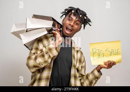 Überraschter afrikanischer, gutaussehender Mann mit Einkaufstasche und gelber Karte mit Big Sale-Aufschrift. Black Friday Stockfoto