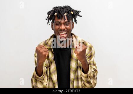 Aufgeregter junger Schwarzer auf Dreadlocks, der die Faust auf weißem Hintergrund hochhebt und Erfolg feiert. Glücklicher afrikanischer Millennial-Mann, der positive Gefühle teilt Stockfoto