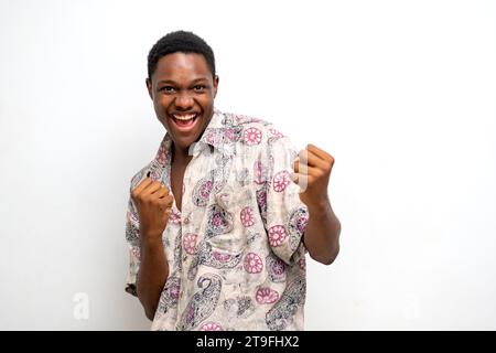Überregter junger Schwarzer, der die Faust auf weißem Hintergrund hochhebt und den Erfolg feiert. Glücklicher afrikanischer Millennial-Mann, der positive Emotionen teilt, Copy Spa Stockfoto