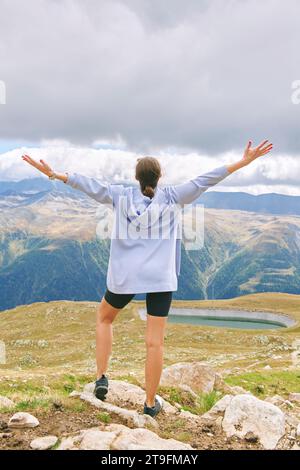 Außenporträt einer glücklichen jungen Frau, die in den Herbstbergen wandert, Rückansicht, weit geöffnete Arme Stockfoto