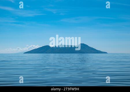 Insel von Afar aus gesehen mit vulkanischen Hügeln, üppiger Vegetation Wald vor einem ruhigen Ozean Stockfoto