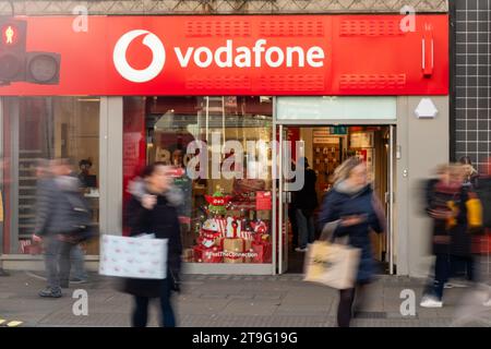 LONDON – 23. NOVEMBER 2023: Vodafone Mobile and Internet High Street Shop and Motion verschwimmen die Käufer auf der Oxford Street, einem Wahrzeichen des Einzelhandels Stockfoto