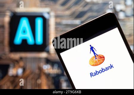 In dieser Fotoabbildung wird das niederländische multinationale Bank- und Finanzdienstleistungsunternehmen Rabobank-Logo auf einem Smartphone mit einem Chip für künstliche Intelligenz (KI) und einem Symbol im Hintergrund dargestellt. Stockfoto