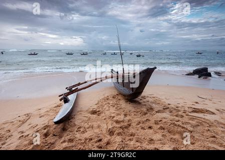 Ein Katamaranboot sitzt am Strand, während andere auf See von lokalen Fischern in Mirissa in Sri Lanka genutzt werden Stockfoto