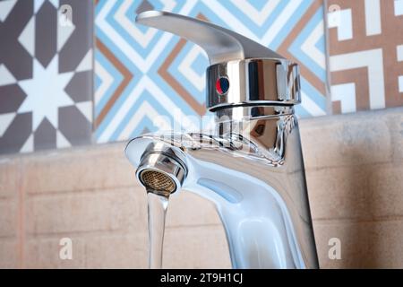 Moderner Chrom-Wasserhahn mit Wasserfluss im Badezimmer, Hintergrund für sanitäre Einrichtungen und Hygienekonzepte Stockfoto