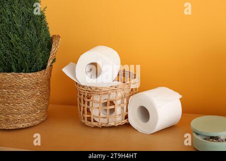 Korb mit Toilettenpapierrollen und Topfpflanze auf Holztisch in der Nähe der Farbwand, Nahaufnahme Stockfoto