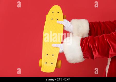 Weihnachtsmann Hände mit gelbem Skateboard auf rotem Hintergrund, Nahaufnahme Stockfoto