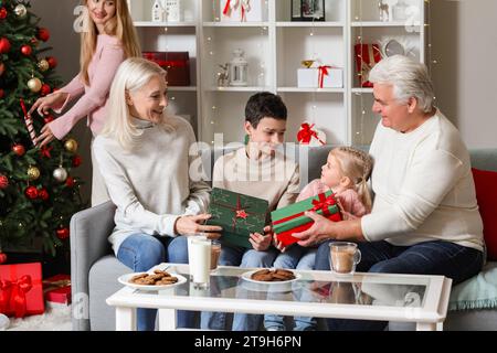 Ein reifes Paar schenkt ihren kleinen Enkeln zu Hause Weihnachtsgeschenke Stockfoto