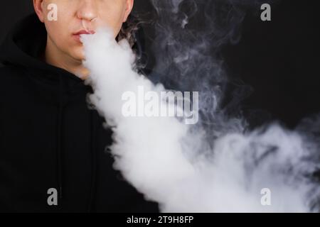 Viel weißer Rauch - Dampf atmet eine Rauchwolke auf dunklem Hintergrund aus, Mann vape selektiver Fokus Stockfoto