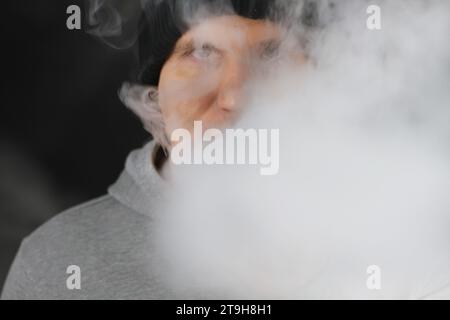 Viel weißer Rauch - Dampf atmet eine Rauchwolke auf dunklem Hintergrund aus, Mann vape selektiver Fokus Stockfoto