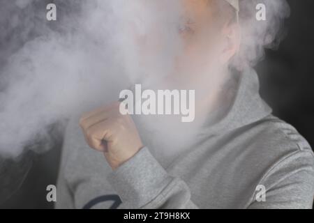 Viel weißer Rauch - Dampf atmet eine Rauchwolke auf dunklem Hintergrund aus, Mann vape selektiver Fokus Stockfoto