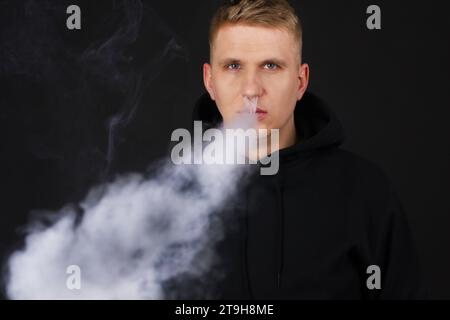 Viel weißer Rauch - Dampf atmet eine Rauchwolke auf dunklem Hintergrund aus, Mann vape selektiver Fokus Stockfoto