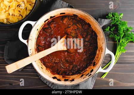 Deutscher Gulasch Simmered in einem emaillierten niederländischen Ofen: Rindfleisch in einer würzigen Tomatensoße in einem gusseisernen Topf mit einem Holzlöffel gekocht Stockfoto