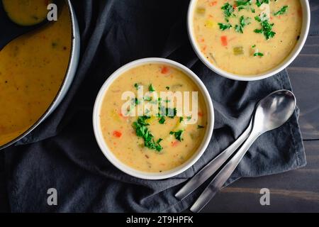Kartoffelsuppe neben einem niederländischen Ofen: Schüsseln mit Gemüsesuppe mit Löffeln neben einem gusseisernen niederländischen Ofen und einer Kelle Stockfoto