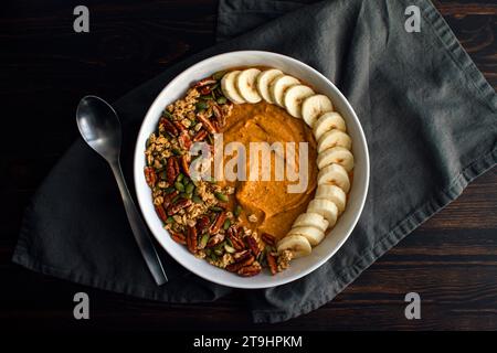 Kürbis Pie Smoothie Schüssel auf einem Holztisch mit Löffel: Kürbis Pie Smoothie mit Müsli, Pekannüssen, Kürbiskernen und in Scheiben geschnittenen Bananen Stockfoto