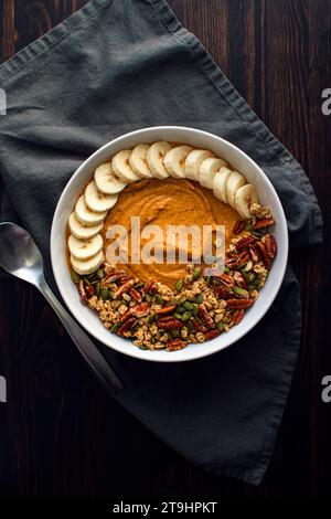 Kürbis Pie Smoothie Schüssel auf einem Holztisch mit Löffel: Kürbis Pie Smoothie mit Müsli, Pekannüssen, Kürbiskernen und in Scheiben geschnittenen Bananen Stockfoto
