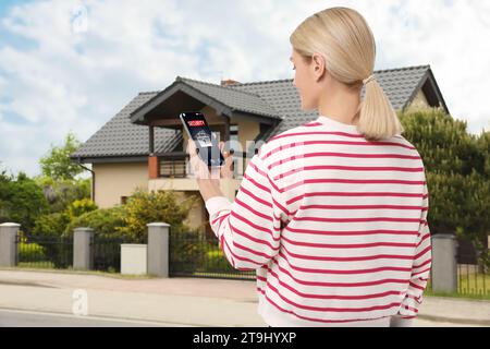 Frau, die im Freien die Anwendung des Haussicherheitssystems auf dem Smartphone verwendet Stockfoto