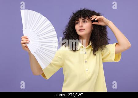 Frau mit Handventilator, die unter Hitze auf violettem Hintergrund leidet Stockfoto