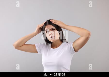 Emotionale Frau, die ihr Haar und ihre Kopfhaut auf grauem Hintergrund untersucht Stockfoto