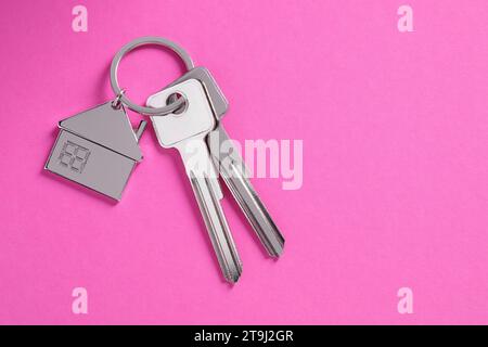 Schlüssel mit Schlüsselanhänger in Form eines Hauses auf rosafarbenem Hintergrund, Draufsicht. Leerzeichen für Text Stockfoto