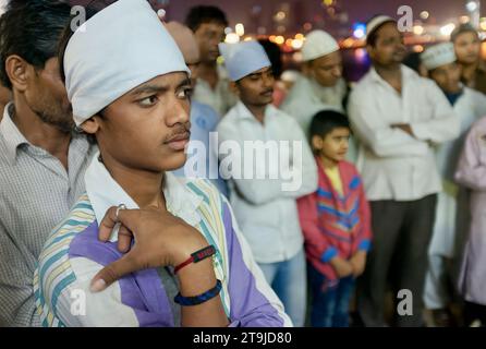 Ein junger muslimischer Mann bei einem abendlichen Besuch der Haji Ali Dargah und der Moschee in Worli, Mumbai, Indien, lauscht Musikern, die Qawwali-Musik aufführen Stockfoto