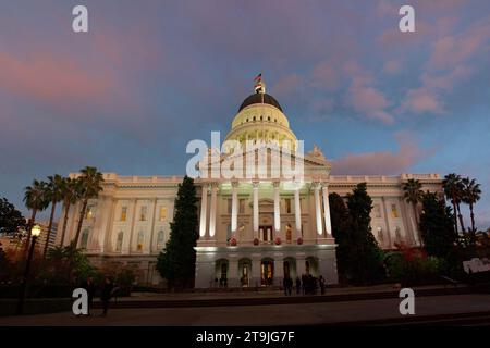 Sacramento, CA - 1. Dezember 2022: Gebäude des Kapitols des Bundesstaats Kalifornien, das mit Weihnachtskränzen dekoriert und für die Feiertage bei Sonnenuntergang mit rosa Wolken beleuchtet ist Stockfoto